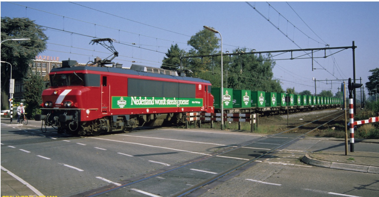 Elektrische locomotief met een rij open wagons met reusachtige kratten erop in Heineken-groen, 1999. Foto: Roland Korving